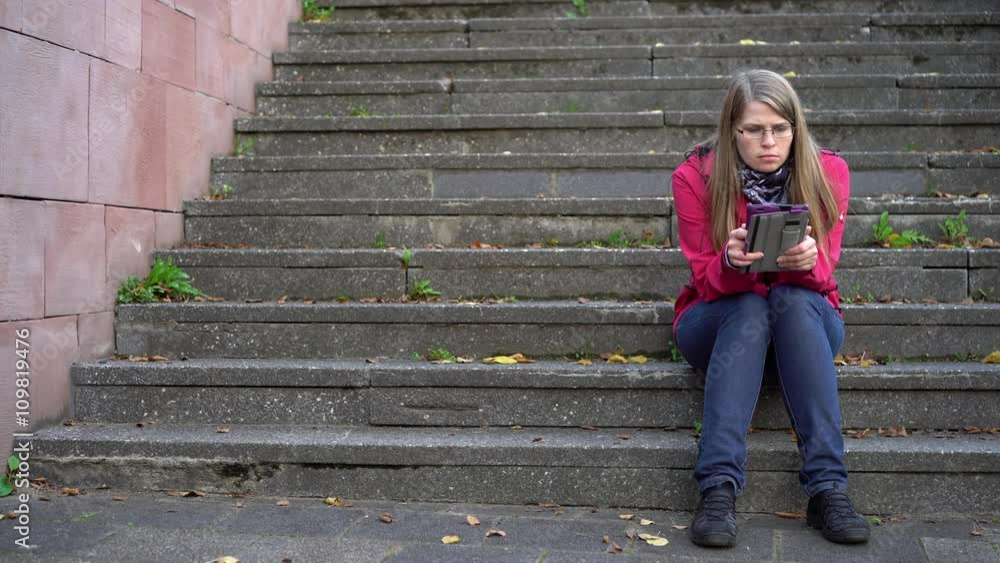 Young girl reading ebook reader on stairs outdoors.
Young girl reading ebook reader on stairs outdoors.