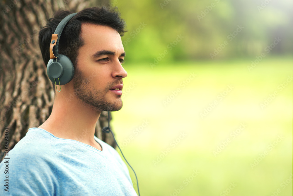 Portrait of beautiful dreaming young man with headphones, listen music on the tree background. Portrait of beautiful dreaming young man with headphones, listen music on the tree background.