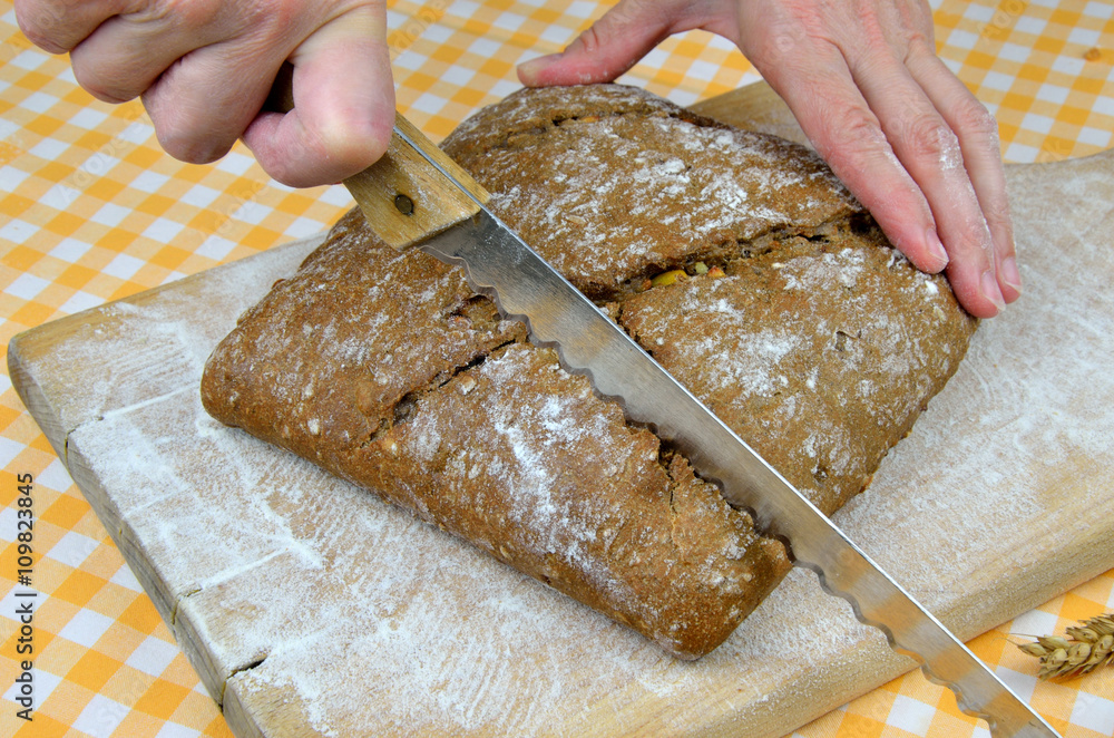 Woman is cutting dark rustic bread with knife Woman is cutting dark rustic bread with knife