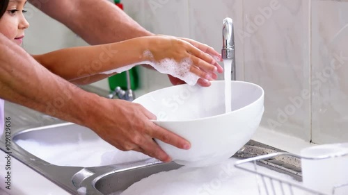 A father is teaching his daughter to wash the dishes