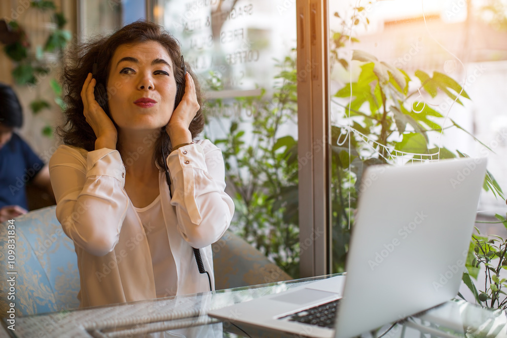 Young Asian girl enjoying music in headphones sitting with a laptop in a cafe. Young Asian girl enjoying music in headphones sitting with a laptop in a cafe.