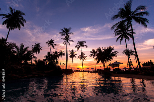 Beautiful twilight on the beach with palm trees reflected in pool.
