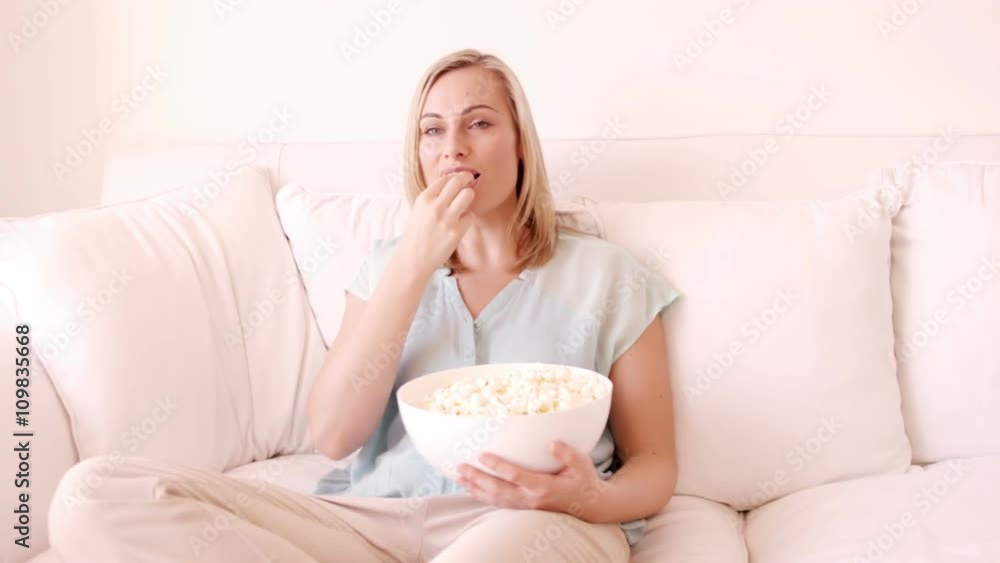 Blonde woman sitting on a sofa and eating popcorn Blonde woman sitting on a sofa and eating popcorn