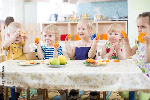 Fotografie Funny kids eating fruits in kindergarten or day care centre