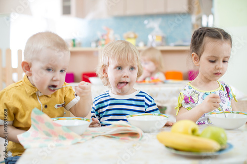 Funny little kids eating from plates in day care centre