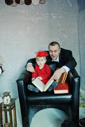 Little cute princess girl with her dad sitting on a chair and re