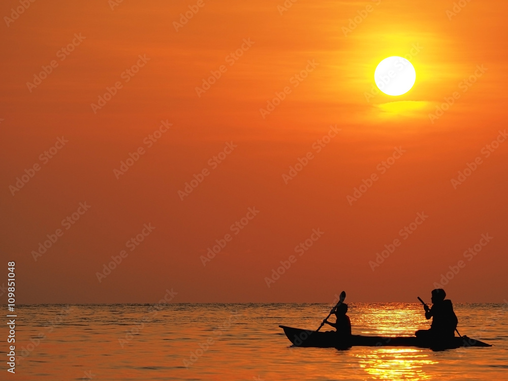 Blur defocus beautiful orange sky sunset above the sea with silhouette of man and boy paddle kayak in sea at Koh Kood, Thailand. Dramatic golden sky at the sunset background.