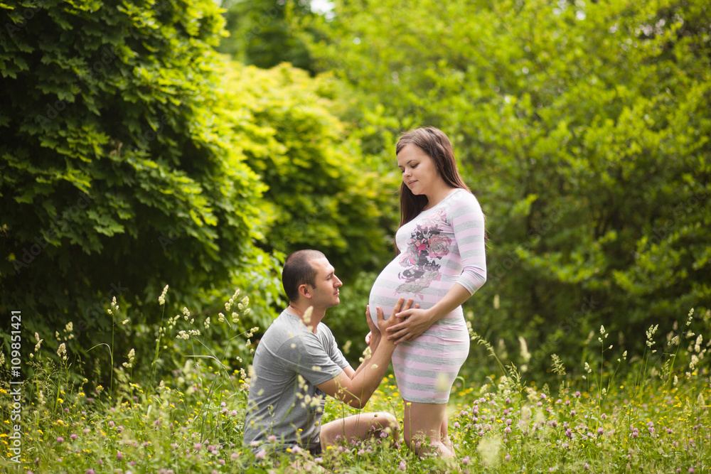Happy couple waiting for baby. Man touches pregnant woman and hugs her belly outdoors in summer. New family concept. Paternity. Happy couple waiting for baby. Man touches pregnant woman and hugs her belly outdoors in summer. New family concept. Paternity.