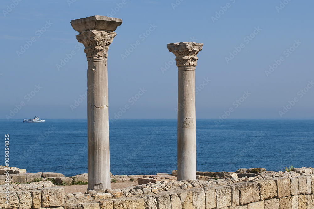 Two marble columns with capitals in ruins of an ancient greek temple with blue sea in background