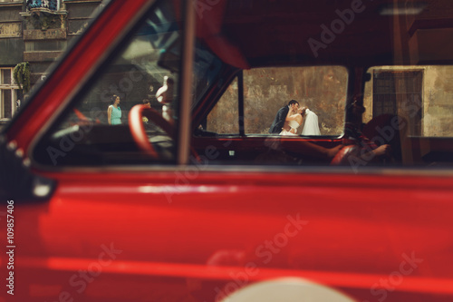Bride and groom kiss behind the car