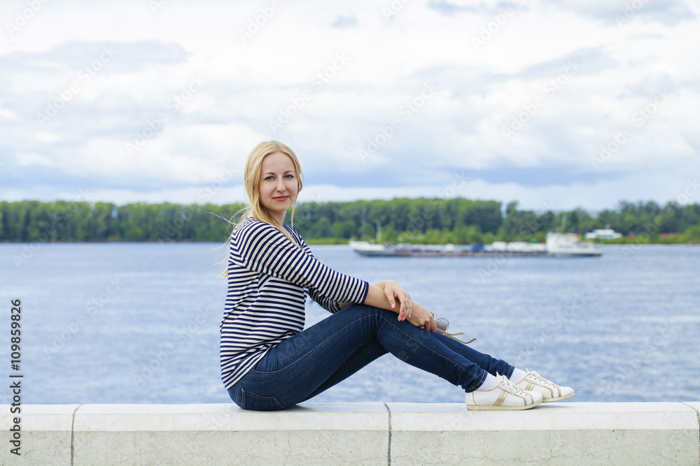 Young beautiful woman in blue jeans sitting in summer street par