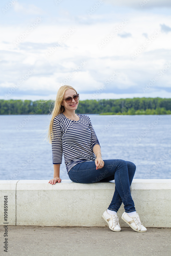 Young beautiful woman in blue jeans sitting in summer street par