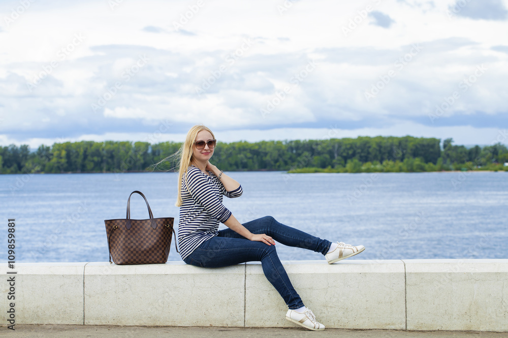 Fototapeta premium Young beautiful woman in blue jeans sitting in summer street par
