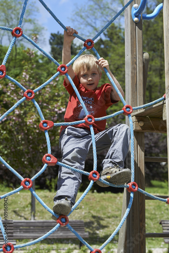 Happy child boy climbed on top of the rope web on playground