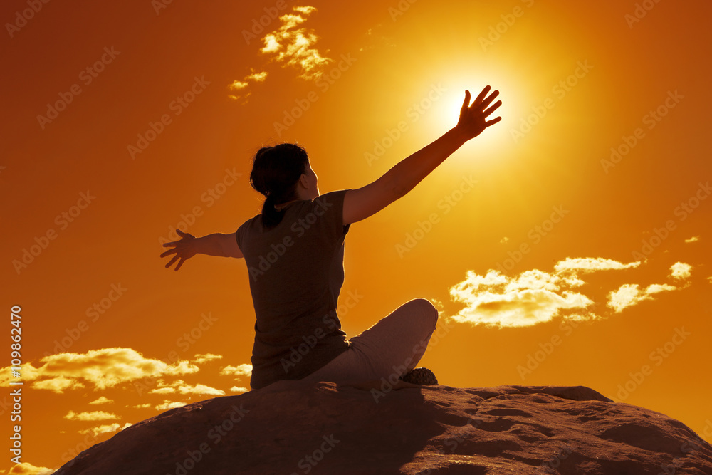 young woman stretching arms sitting on a rock at sunset