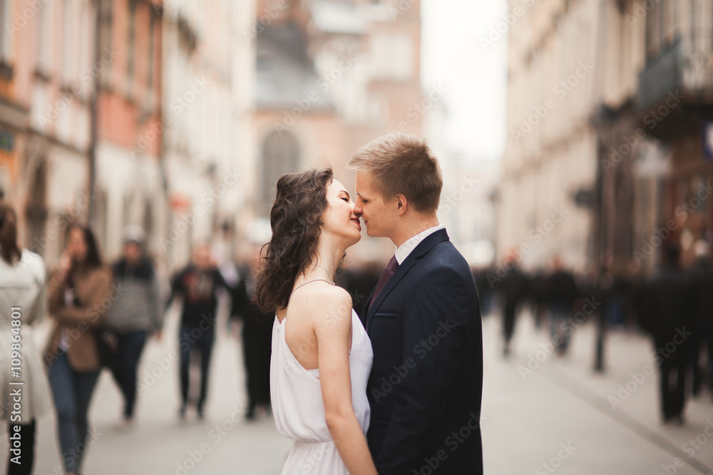 Gorgeous wedding couple, bride, groom kissing and hugging standing in the crowd Gorgeous wedding couple, bride, groom kissing and hugging standing in the crowd