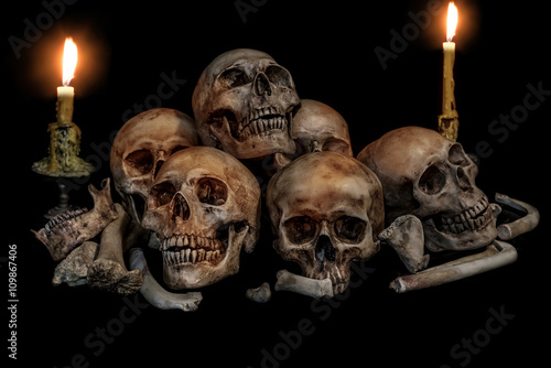 Pile of skulls and bones with two candles on black background. Genocides concept still life style.
