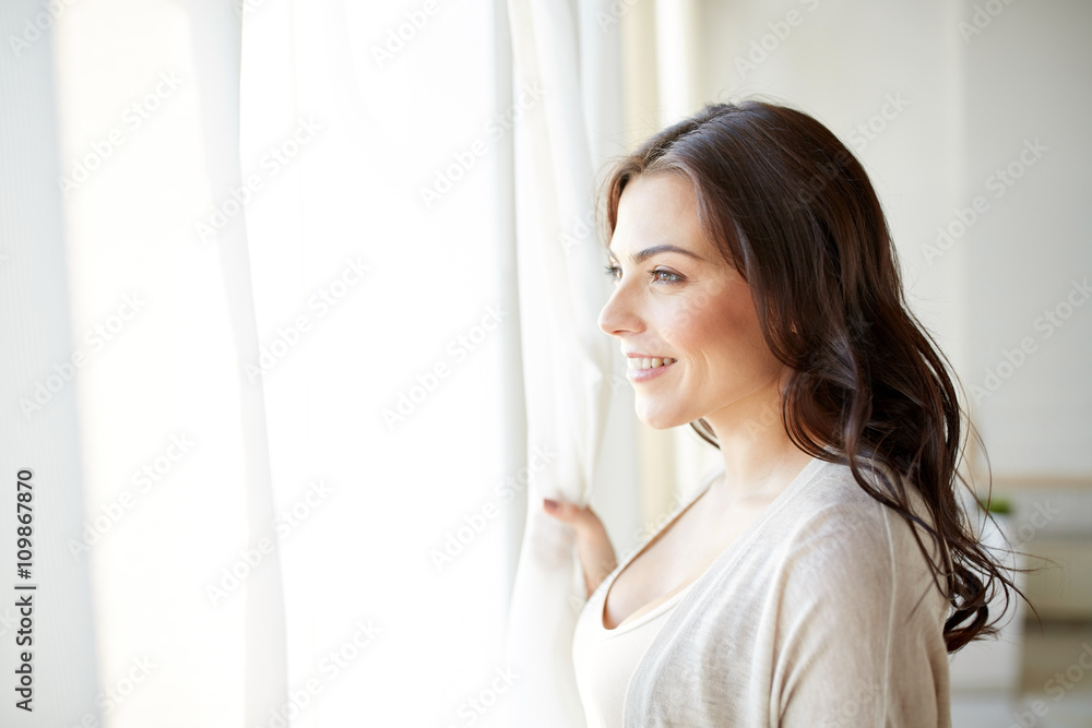 happy young woman looking through window at home