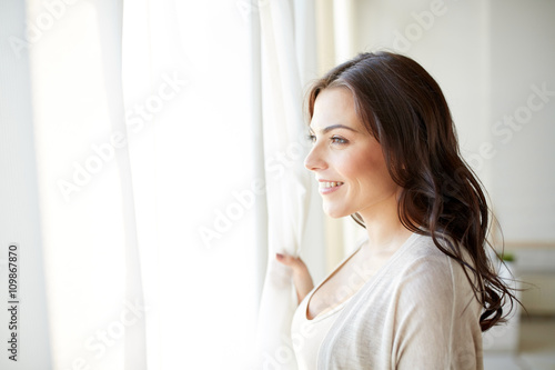 happy young woman looking through window at home