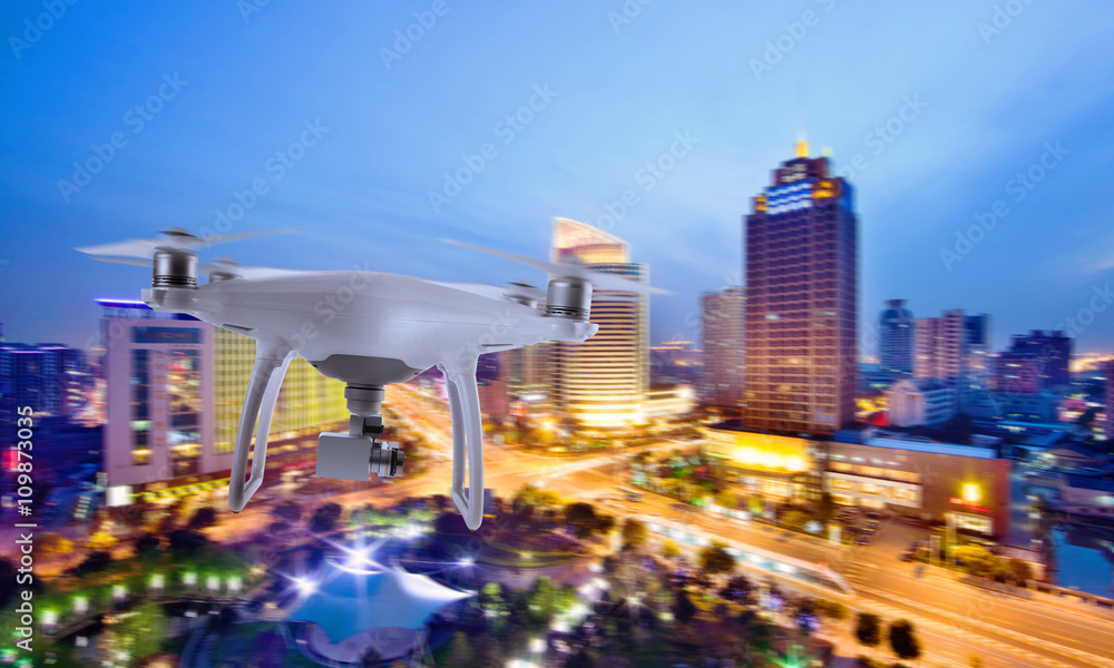 Drone quad copter with camera flying over the city center in night.