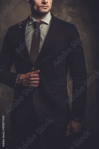 Serious well-dressed hispanic man posing on dark background.