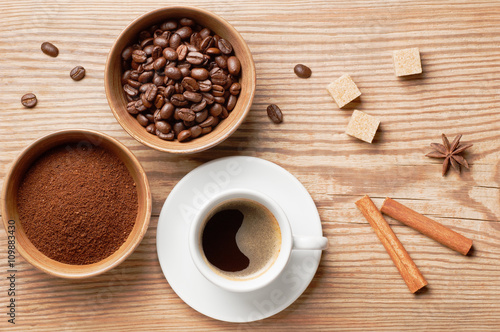 Coffee beans, ground coffee and cup of coffee on rustic wooden table decorated spices, sugar and coffee beans, top view