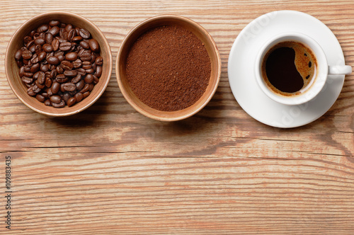 Coffee beans, ground coffee and cup of brewwed coffee on rustic wooden table, top view with space for text