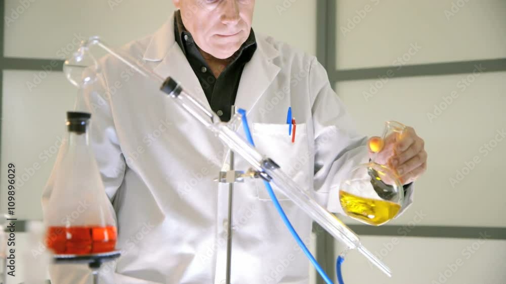 A chemist standing behind the condenser tubes of a distillation kit ...