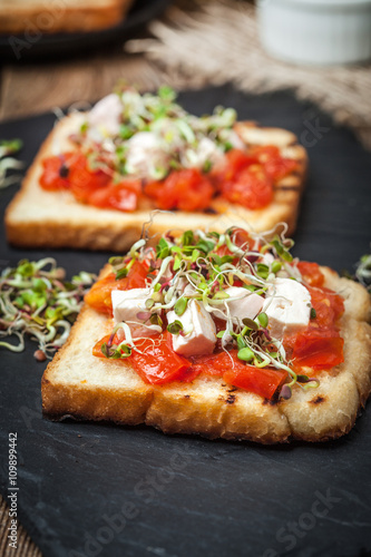 Grilled toasted bread with roasted tomatoes, feta cheese and radish sprouts.