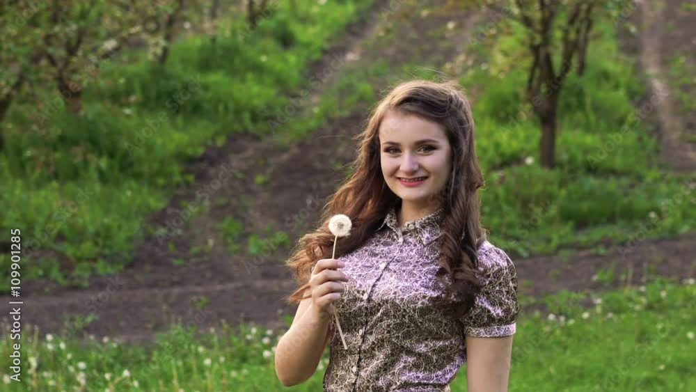 Young model blowing dandelion in the garden and smiling. Slowly Young model blowing dandelion in the garden and smiling. Slowly