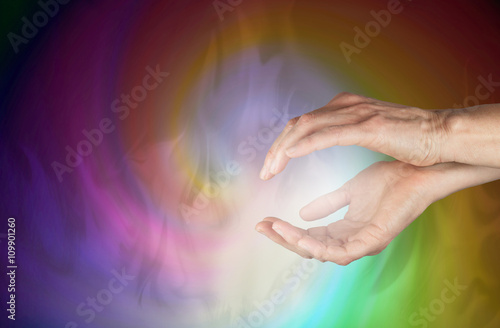 Sensing healing energy field - female cupped hands  with an ethereal spiraling multicolored energy field flowing outwards and soft white smoke effect