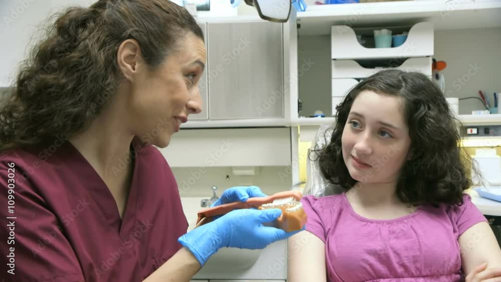 A dental hygienist using a dental model and toothbrush shows her young