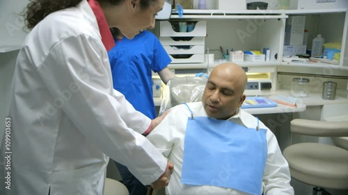 A friendly female dentist enters the exam room and greets her patient who is waiting in the dental chair. photo