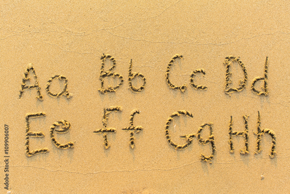 Alphabet written by hand on sandy beach (letters from A to H)