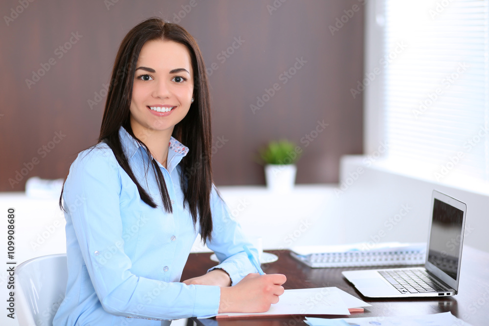 Young business woman sitting and writing at the table in office Young business woman sitting and writing at the table in office