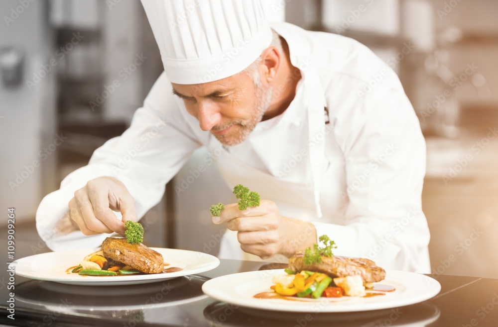 Concentrated male chef garnishing food in kitchen Concentrated male chef garnishing food in kitchen