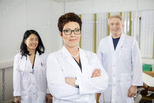 Doctor Standing Arms Crossed While Colleagues Smiling In Clinic