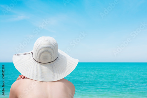 Young woman in swimsuit and hat on the beach looking into distan