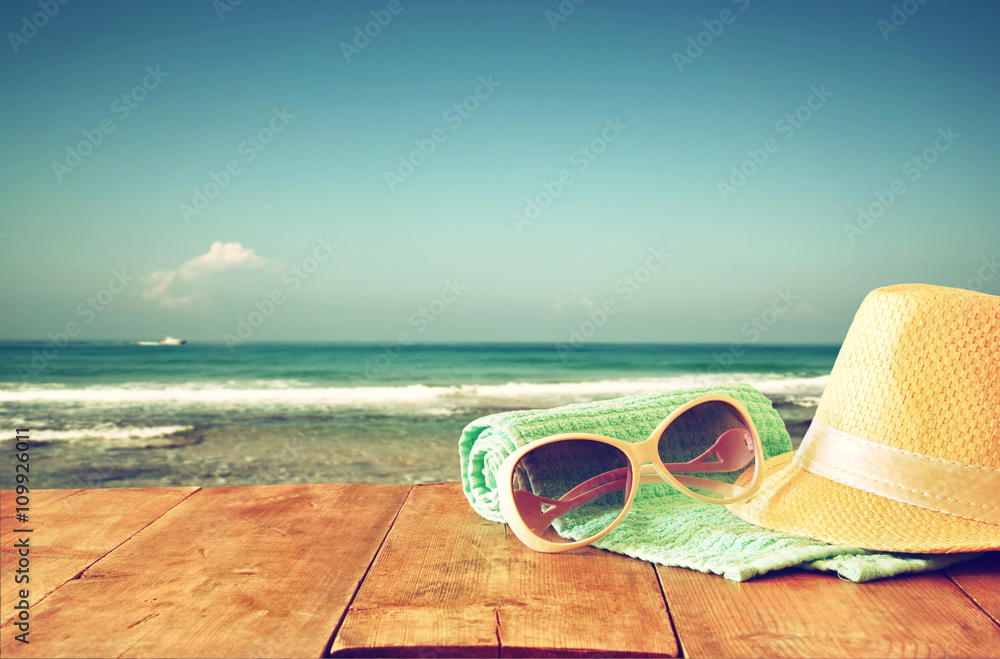 fedora hat and sunglasses over wooden table and sea landscape