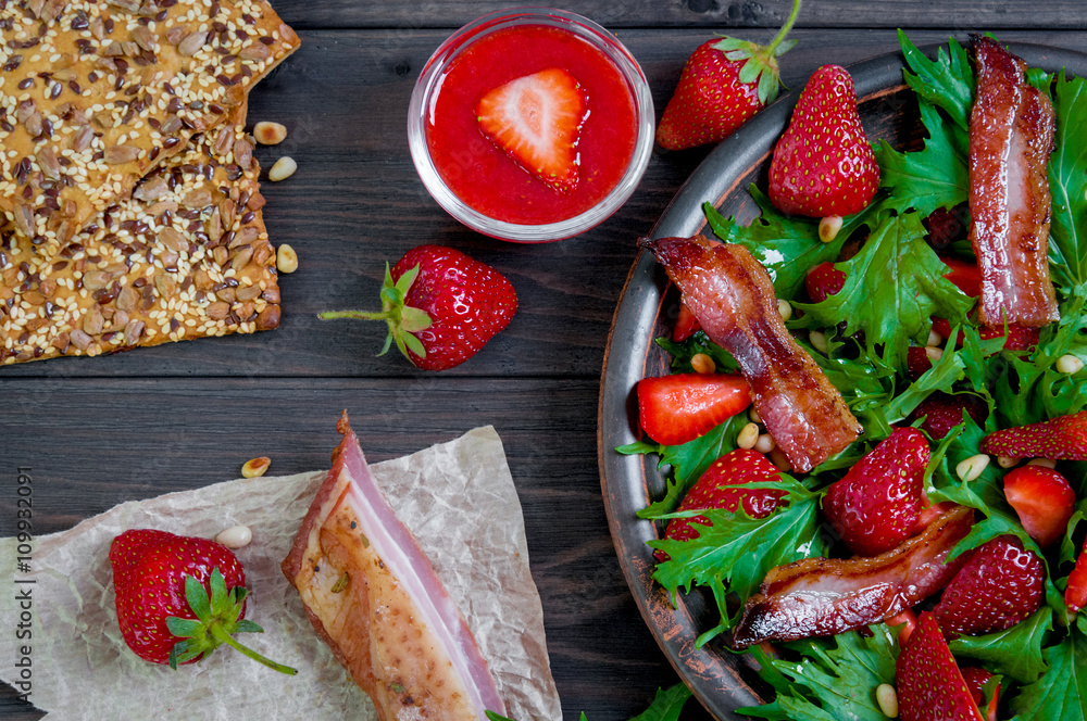 Useful strawberry salad with arugula, nuts and bacon, berry sauce
