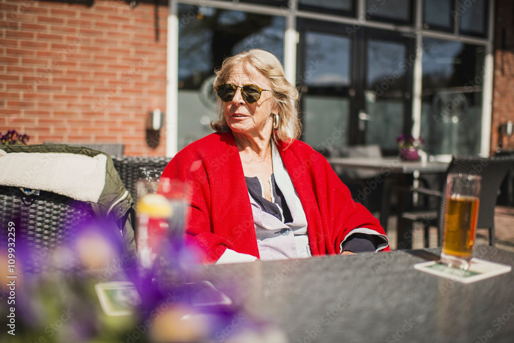 Senior blonde woman with sunglasses sitting at outdoor cafe