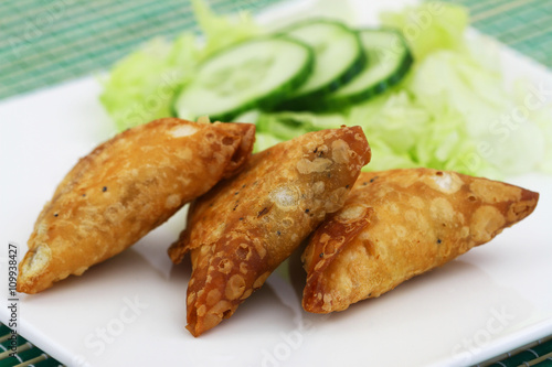 Indian samosas with green lettuce and slices of cucumber on the side, closeup
