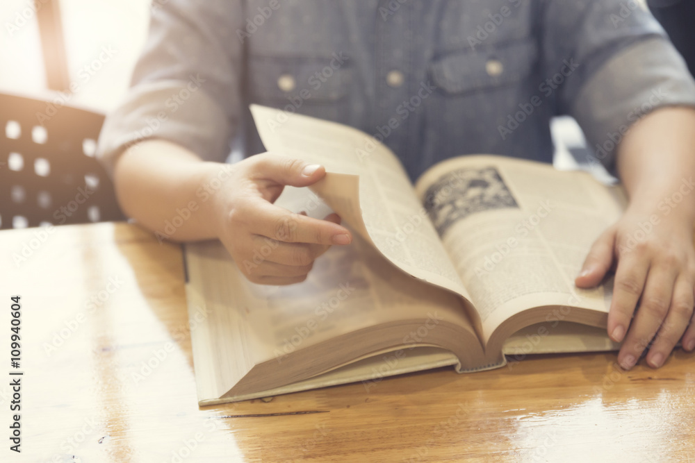 woman's hand reading book on wooden table woman's hand reading book on wooden table