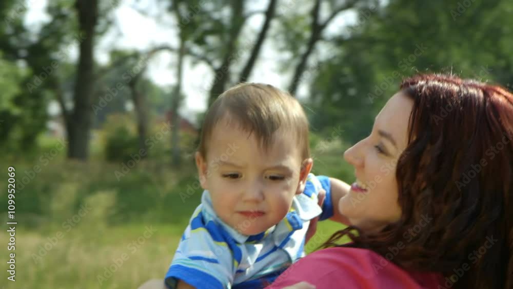 A smiling young mother outdoors on a bright sunny morning playfully lifts her cute two year old son into the air. A smiling young mother outdoors on a bright sunny morning playfully lifts her cute two year old son into the air.