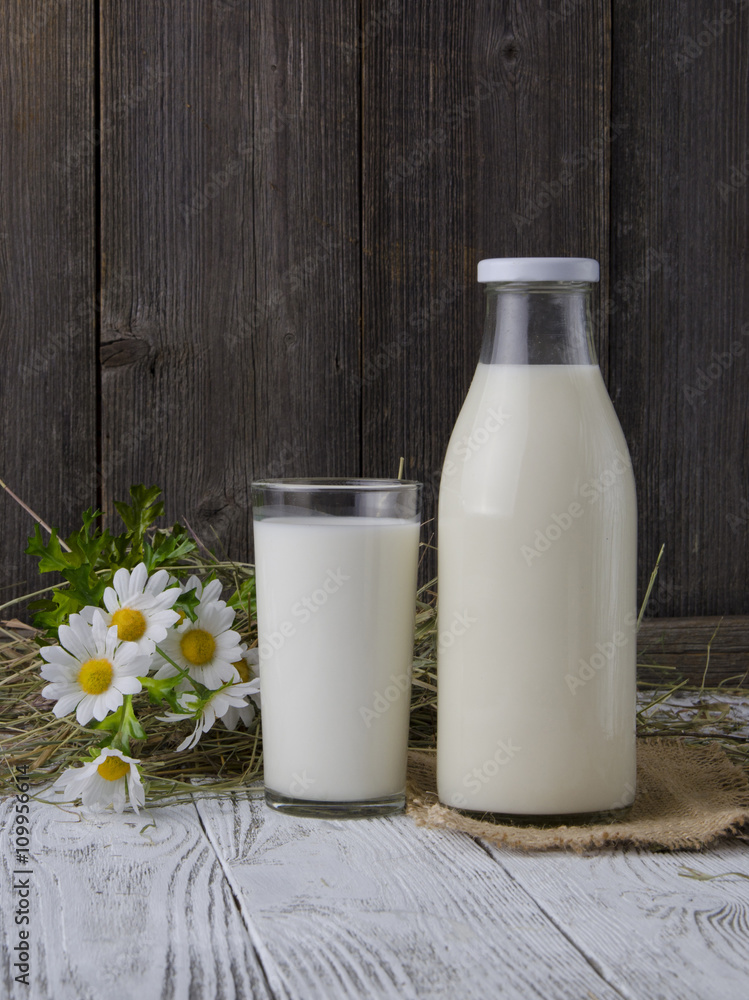 A bottle of rustic milk and glass of milk on a wooden table A bottle of rustic milk and glass of milk on a wooden table