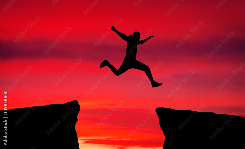 Man jumping across the gap from one rock to cling to the other.