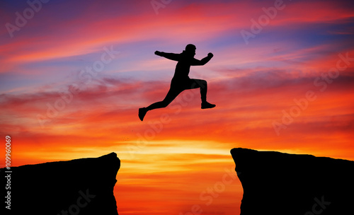 Man jumping across the gap from one rock to cling to the other.