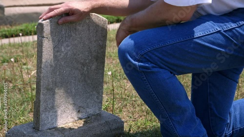 A grieving man walks into the scene and kneels by an old worn faded gravestone