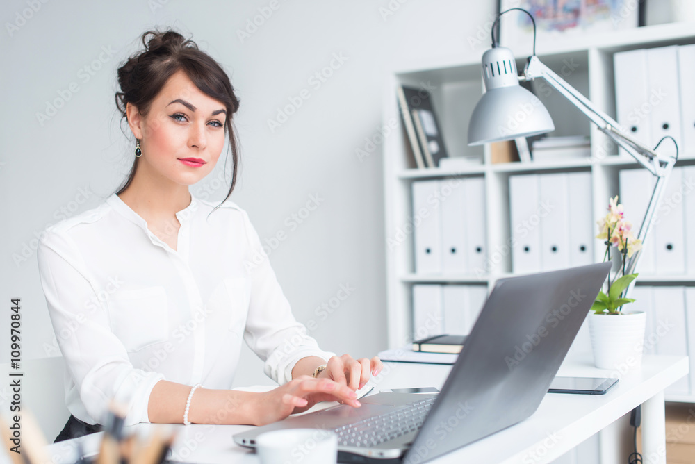 Close-up portrait of a businesswoman at her workplace working with pc, looking in camera, wearing office suit. Close-up portrait of a businesswoman at her workplace working with pc, looking in camera, wearing office suit.