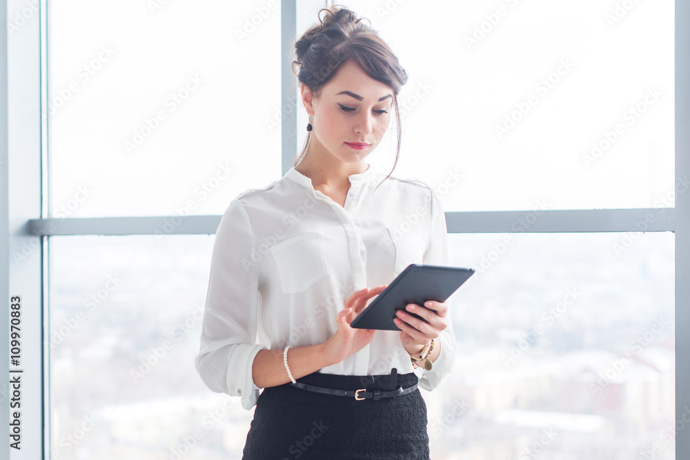 Close-up portrait of a young woman, office worker standing near her workplace, using tablet at break time, reading news, surfing the internet. Close-up portrait of a young woman, office worker standing near her workplace, using tablet at break time, reading news, surfing the internet.